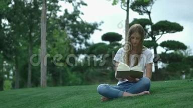 公园里年轻漂亮的女孩正在看书。一个学生正在翻阅一本书。坐在草地上